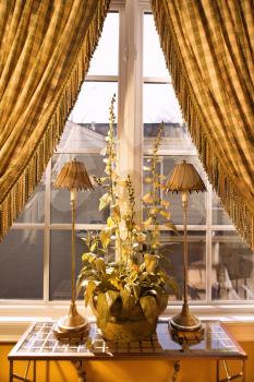 Royalty Free Photo of a Window With Curtains Pulled Back and Decorative Table With Lamps and a Plant