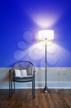Royalty Free Photo of a Blue Projection Light on a Wall With a Bright Floor Lamp and Open Book on a Chair