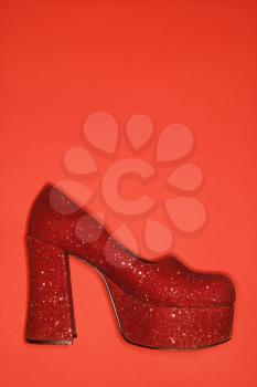 Red glitter high heel shoe against red background.