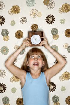 Caucasian female child holding clock over head.