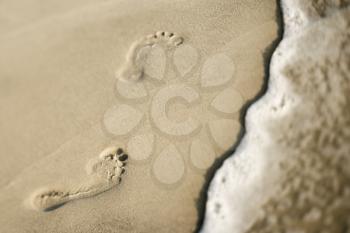 Royalty Free Photo of Footprints in the Sand Next to a Wave