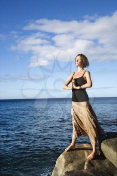 Caucasian young adult female meditating by the Pacific ocean of Maui, Hawaii.