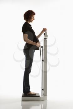 Side view of pregnant Caucasian mid-adult woman reading her weight on scale.