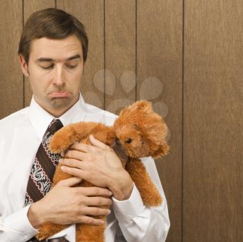 Mid-adult Caucasian male holding a stuffed animal looking sad.