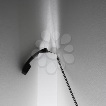Royalty Free Photo of a Receiver of a Corded Telephone Resting on Sconce Lighting on a Wall