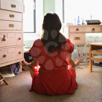 Royalty Free Photo of a Back View of a Woman in a Red Robe Sitting on the Floor Meditating in Lotus Pose