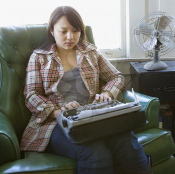 Royalty Free Photo of a Woman Sitting in a Green Chair Typing on a Typewriter