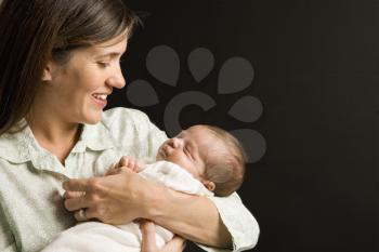 Mother smiling holding sleeping baby against black background.