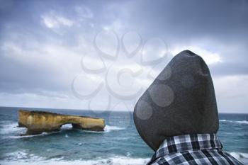 Royalty Free Photo of a Person Wearing a Hood Facing a Rock Formation as Seen from Great Ocean Road in Australia