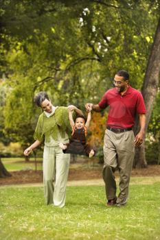 Royalty Free Photo of a Mother and Father Swinging a Toddler Holding His Hands in a Park