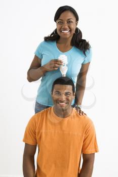 African American female holding energy-saving lightbulb over  man's head.
