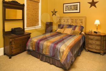Bed with striped bedspread and dresser in the bedroom of an affluent home. Horizontal shot.