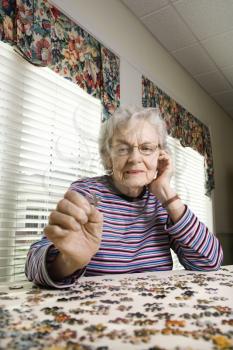 Elderly woman concentrating and holding a jigsaw puzzle piece. Vertical shot.