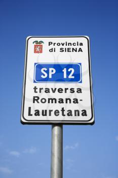 Low angle view of an Italian road sign against blue sky. Vertical shot.