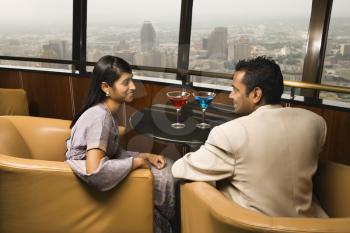 Young adult male and female seated near window in a high rise restaurant. They are smiling at one another. Horizontal shot.