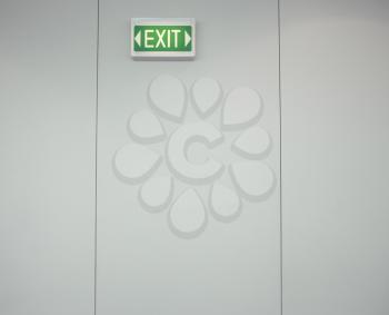 Low angle view of a green, lighted exit sign on a gray wall. Horizontal shot.