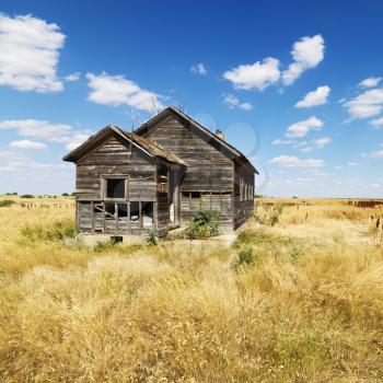 Abandoned house in state of disrepair in field in rural North Dakota. Square format.