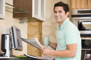 Royalty Free Photo of a Man at a Computer Holding a Newspaper