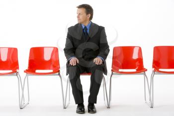 Royalty Free Photo of a Businessman Sitting in a Row of Empty Chairs