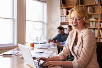 Businesswoman Using Laptop At Desk In Busy Office