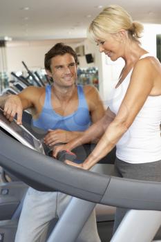 Senior Woman Working With Personal Trainer On Running Machine In Gym