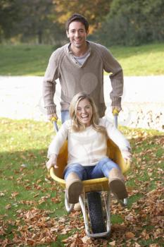 Man pushing wife through autumn leaves on wheelbarrow