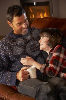 Father And Son Relaxing With Hot Drink By Cosy Log Fire