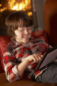 Young Boy Relaxing With Tablet Computer By Cosy Log Fire