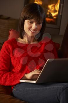 Middle Aged Woman Using Laptop Computer By Cosy Log Fire