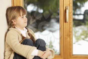 Young Girl Sitting On Window Ledge Looking At Snowy View