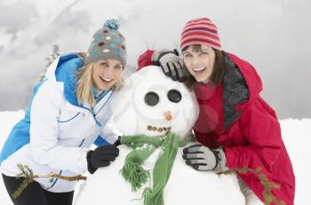 Two Female Friends Building Snowman On Ski Holiday In Mountains