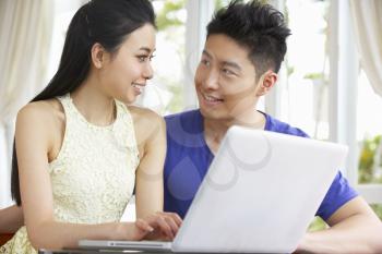 Young Chinese Couple Sitting At Desk And Using Laptop At Home