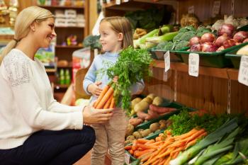 Mother And Daughter Choosing Fresh Vegetables In Farm Shop