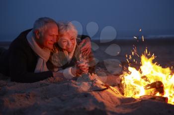 Senior Couple Sitting By Fire On Winter Beach