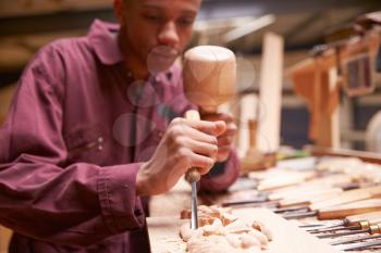 Apprentice Using Chisel To Carve Wood In Workshop