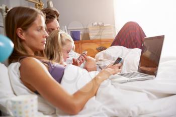 Family Lying In Bed Together Using Digital Devices