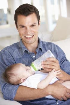 Young Father With Baby Feeding On Sofa At Home