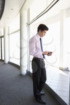 Young Businesman Standing In Corridor Of Modern Office Building Using Mobile Phone
