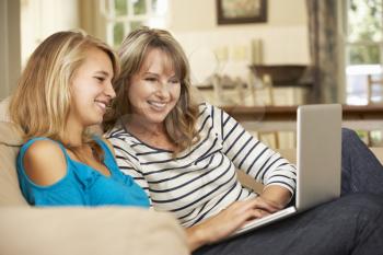 Mother With Teenage Daughter Sitting On Sofa At Home Using Laptop