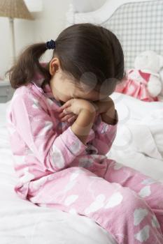 Tired Young Girl Wearing Pajamas Sitting On Bed