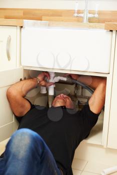A plumber lying on his back to fix a kitchen sink, vertical