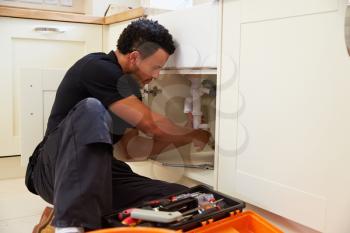 Mixed race plumber fixing the kitchen sink in a home