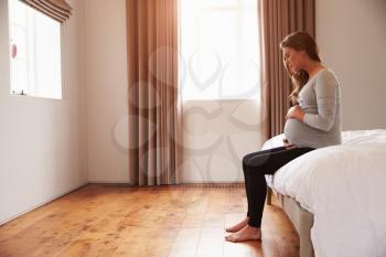 Pregnant Woman Sitting On Bed Holding Belly