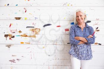 Portrait Of Female Artist Against Paint Covered Wall