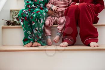 Three Children In Pajamas Sitting On Stairs At Christmas