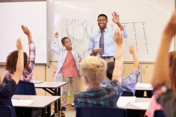 Teacher and pupil with raised hands at front of school class