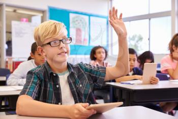 Boy with glasses raising hand in elementary school class