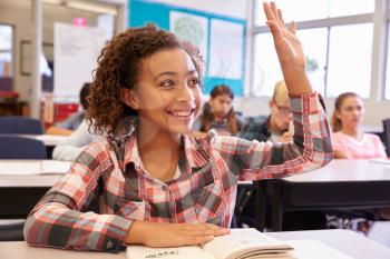 Schoolgirl at desk in elementary school raising her hand
