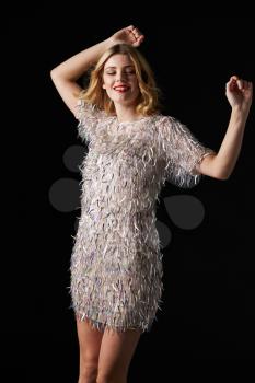 Glamorous blonde woman dancing with arms raised, on black