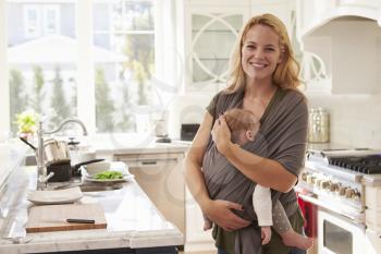 Portrait Of Busy Mother With Baby In Sling At Home